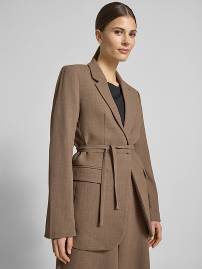 Vrouwenmodel draagt blazer met viscose van MSCH Copenhagen, materiaalmix, getailleerde pasvorm, reverskraag, klepzakken, model 'Darina', knoopsluiting, tailleband, kleur bruin, gladde textuur, borstwijdte 48 cm, ruglengte 72 cm, mouwlengte 63 cm, detailopname bovenlichaam.