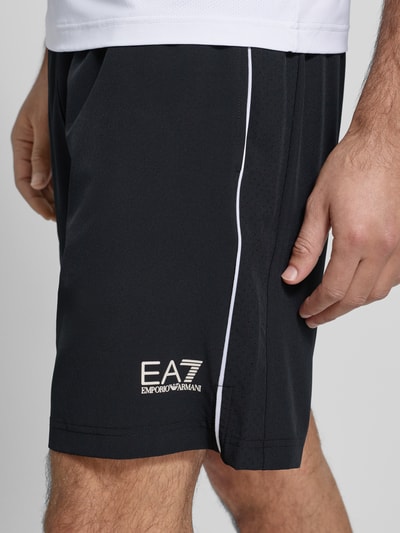 Männermodel trägt Shorts mit elastischem Bund und Logo von EA7 Emporio Armani, Schwarz mit weißem Logo, Material-Mix mit Stretch-Anteil, Nahaufnahme Oberschenkel.