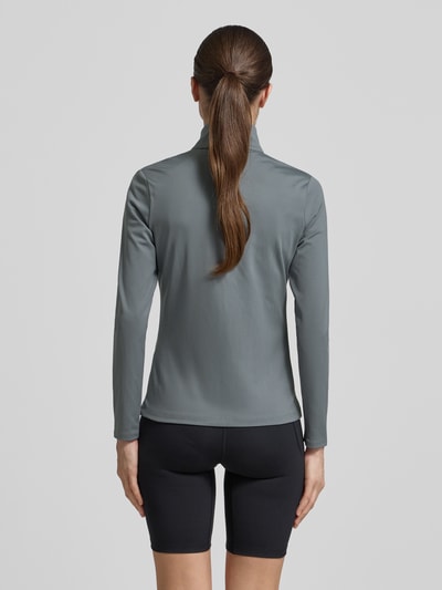 Vrouwenmodel draagt trainingsjack met opstaande kraag en logo van Under Armour in grijs, materiaalmix met stretch, slim fit, steekzakken, ruglengte maat S 59 cm, schouderbreedte 35 cm, borstwijdte 43 cm, mouwlengte 60 cm, geheel van achteren.