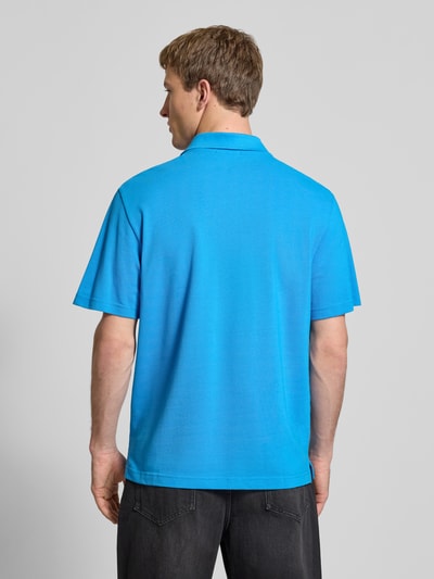 Männermodel trägt Easy Fit Poloshirt mit Polokragen von Calvin Klein Jeans in Blau, reine Baumwolle, Label-Stitching, Ganzkörperansicht Rückansicht. Rückenlänge bei Größe M: 71 cm.