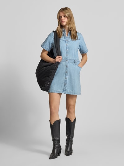 Frauenmodel trägt Regular Fit Jeanskleid aus reiner Baumwolle von Levi's®, hellblauer Denim, kurze Ärmel, V-Ausschnitt, sichtbare Nähte, Knopfleiste, 5-Pocket-Design, Mini-Länge, stoffliche Struktur leicht, Ganzkörperansicht von vorne.