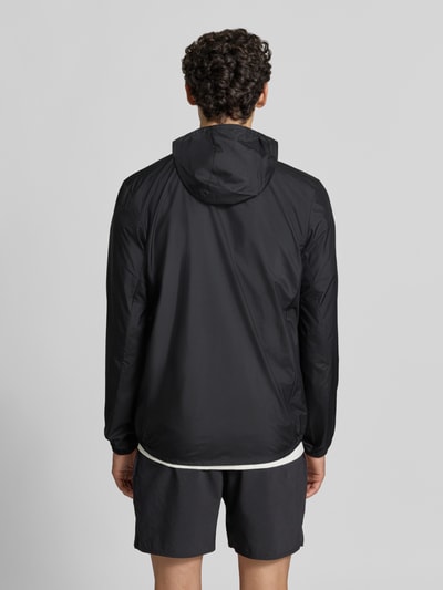 Männermodel trägt schwarze Regular Fit Trainingsjacke mit Logo-Print Modell 'Core' von ASICS TIGER, glatte Struktur, Ganzkörperansicht Rückansicht.