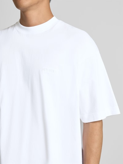 Männermodel trägt Oversized T-Shirt aus reiner Baumwolle von VETEMENTS, Weiß, Label-Stitching, Stehkragen, Nahaufnahme Oberkörper.