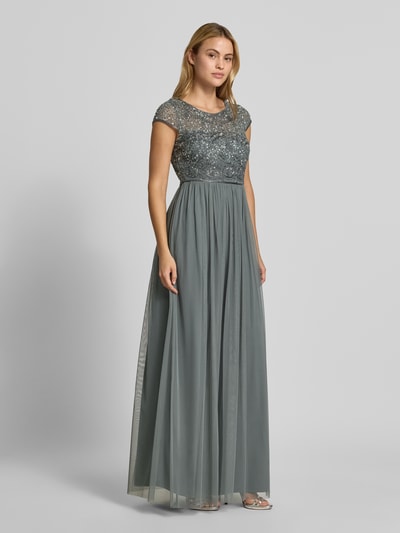 Modelka nosi sukienkę wieczorową 'Abendkleid mit Pailletten' od Christian Berg Cocktail, taliowany krój, okrągły dekolt, cekiny, obszycie ozdobnymi kamieniami, zamek błyskawiczny z tyłu, długość tyłu w rozmiarze 36: 34 cm, szerokość w rozmiarze 36: 40 cm, długa, zwiewna spódnica, stonowane odcienie szarości, widoczne różne faktury tkanin, całość z przodu, całopostaciowa perspektywa.