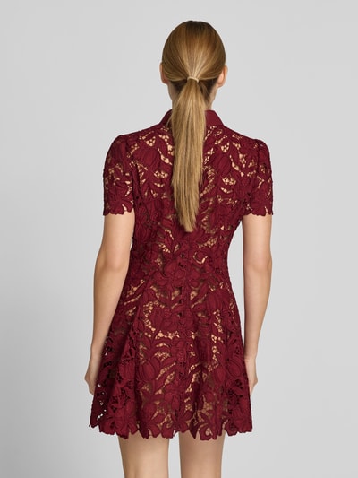 Frauenmodel trägt Minikleid mit Allover-Spitzenbesatz von Self-Portrait in Bordeauxrot, tailliert, blickdicht unterlegt, Rückansicht.