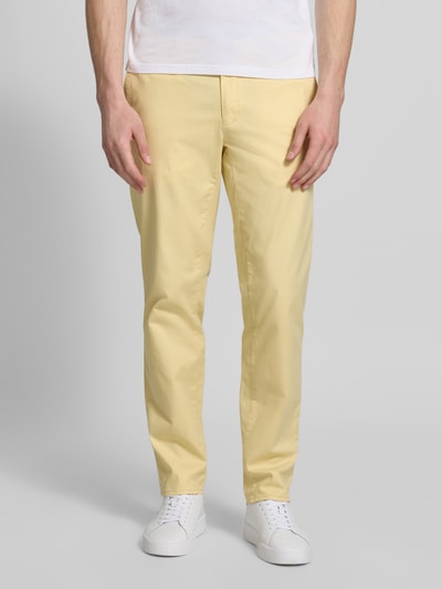 Mężczyznamodel nosi spodnie materiałowe Brax Slim Fit Stoffhose mit Gesäßtaschen Modell 'Fabio' z mieszanki bawełny, krój slim fit, wpuszczane kieszenie, kieszonka na monety, szerokość w rozmiarze 32/32: 44 cm, długość wewnętrzna nogawki: 81 cm, jasny żółty kolor, tekstura gładka, Ganzkörperansicht z przodu.