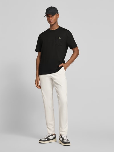 Männermodel trägt Regular Fit T-Shirt aus reiner Baumwolle von Lacoste, unifarben Schwarz, Logo-Stitching, Ganzkörperansicht von vorne.