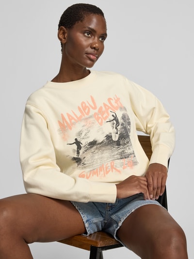 Frauenmodel trägt Relaxed Fit Sweatshirt mit Foto-Print von Anine Bing aus reiner Baumwolle, Statement-Print, elastische Abschlüsse, Rückenlänge bei Größe S 56 cm, helle Farben, Ganzkörperansicht von vorne.