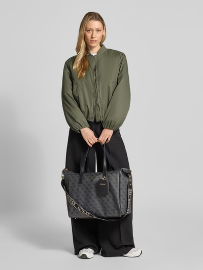 Frauenmodel trägt Damen Shopper mit Logo-Muster Modell 'LATONA CARRYON' von Guess mit Hauptfach und Schulterriemen, Ganzkörperansicht von vorne.