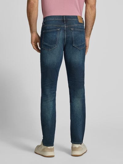 Männermodel trägt Modern Fit Jeans aus Baumwoll-Mix Modell 'Chuck' von Brax in Mid Waist Denim-Optik, Ganzkörperansicht Rückansicht.