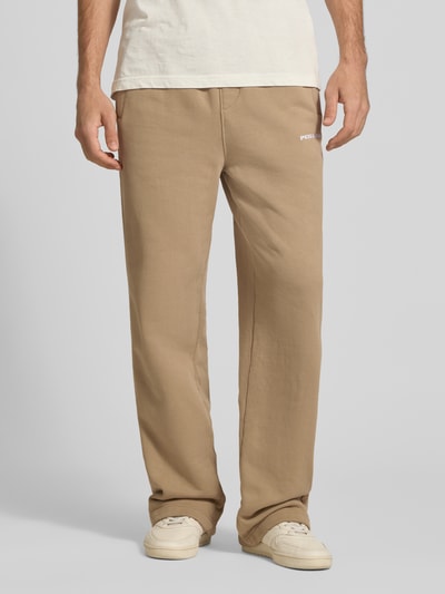 Männermodel trägt Loose Fit Sweatpants aus Baumwoll-Mix mit Label-Detail von PEGADOR, beiger Farbton, Eingrifftaschen, elastischer Bund, Ganzkörperansicht von vorne.