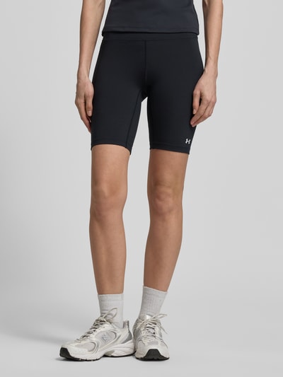 Frauenmodel trägt Radlerhose mit Logo von Under Armour in Schwarz mit körpernaher Passform, Material-Mix mit Stretch-Anteil, Nahaufnahme Unterkörper.