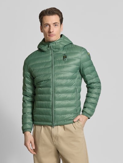 Männermodel trägt grüne Steppjacke mit Zweiwege-Reißverschluss Modell 'Charles' von Blauer Usa, Regular-Fit, Kapuze, Label-Detail, Ganzkörperansicht von vorne. Rückenlänge 65 cm, Schulterbreite 47 cm, Brustweite 55 cm, Ärmellänge 65 cm.