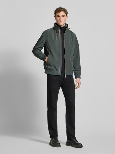 Männermodel trägt Regular Fit Jacke mit Kapuze Modell 'Como' von NAUTGÅRD in Dunkelgrün mit Reißverschlusstaschen, Ganzkörperansicht von vorne.