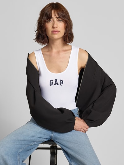 Frauenmodel trägt Tanktop mit Logo-Print und Rundhalsausschnitt von GAP in Weiß, Feinripp, körpernah, Baumwoll-Mix, Nahaufnahme Oberkörper.