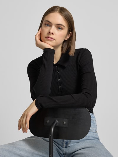 Vrouwenmodel draagt Slim Fit Langarmshirt uit katoenmix model 'KITTE' van Pieces, effen zwart, ribstructuur, polokraag, label stitching, long sleeves, vooraanzicht bovenlichaam.