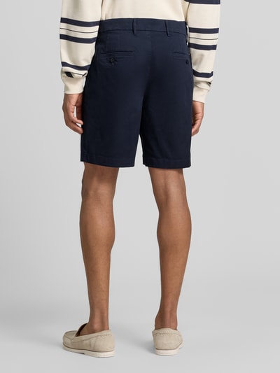Männermodel trägt Chinoshorts aus Baumwoll-Mix Modell 'DOVER' von Tommy Hilfiger, Optik: Unifarben, Passform: Regular-Fit, Zwei Paspeltaschen mit Knopf hinten, Farbe Dunkelblau, feine glatte Textur, Ganzkörperansicht Rückansicht.