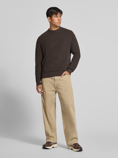 Männermodel trägt Regular Fit Strickpullover aus reiner Baumwolle von REVIEW in Dunkelbraun, Rundhalsausschnitt, Ganzkörperansicht von vorne.
