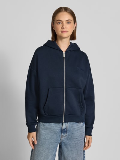 Frauenmodel trägt Relaxed Fit Basic Sweatjacke mit Kapuze von REVIEW in Dunkelblau, Baumwoll-Mix, Logo-Print, Kängurutasche, Ganzkörperansicht von vorne.