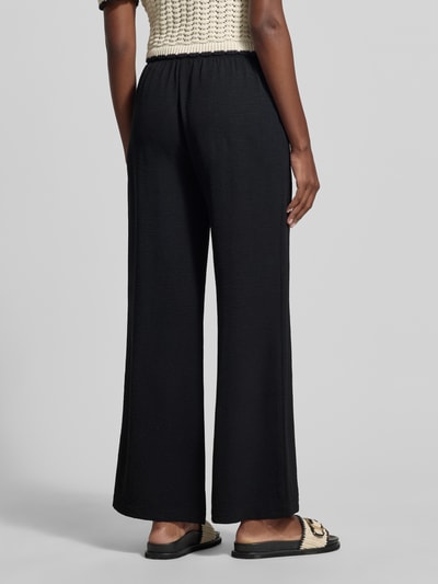 Frauenmodel trägt schwarze Stoffhose mit Strukturmuster von Christian Berg Woman, Relaxed Fit, Tunnelzug, Eingrifftaschen, Ganzkörperansicht Rückansicht.