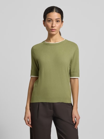 Modelka nosi Regular Fit Strickpullover mit Rundhalsausschnitt von More & More, zielony kolor, półrękaw, miękka tekstura, krój regular fit, mieszanka wiskozy, elastyczne wykończenia; widok całej sylwetki z przodu.