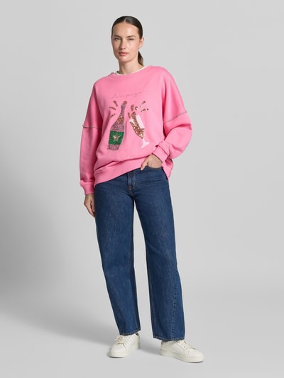 Frauenmodel trägt Oversized Sweatshirt aus reiner Baumwolle von miss goodlife in Pink mit Pailettenbesatz, Statement-Stitching und elastischen Abschlüssen, Ganzkörperansicht von vorne.