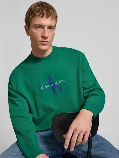 Männermodel trägt Sweatshirt mit Rundhalsausschnitt und Logo von Calvin Klein Jeans, grün, Reine Baumwolle, Regular-Fit, Nahaufnahme Oberkörper.