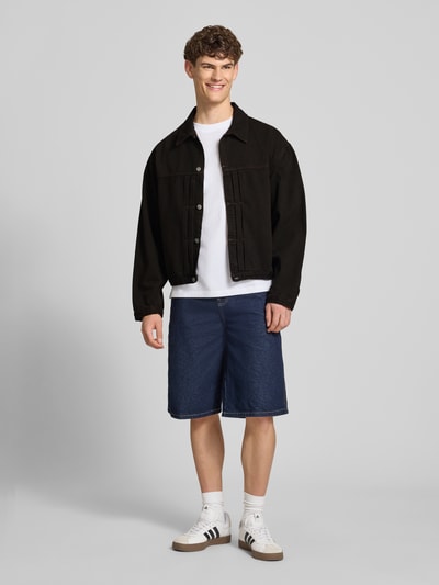 Männermodel trägt schwarze Jeansjacke mit Knopfleiste Modell 'FREELAND' von Edwin aus Reine Baumwolle, Relaxed-Fit, Ganzkörperansicht von vorne.