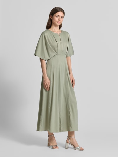 Vrouwenmodel draagt Midikleid met V-hals model 'VIANNA' van Copenhagen Muse, getailleerd fit, plooien, zachte groene tint, gladde textuur, volledig lichaamsbeeld van voren. Ruglengte maat S: 130 cm, borstbreedte: 40 cm, mouwlengte: 28 cm.