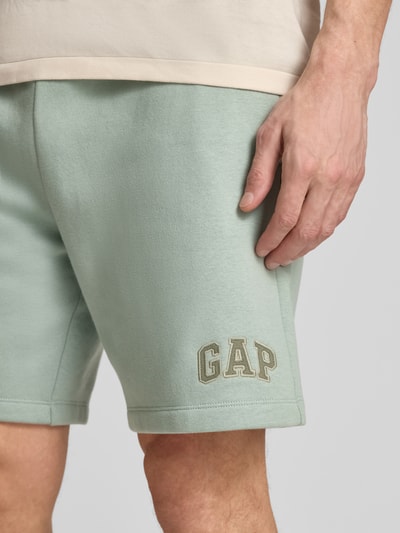 Männermodel trägt Sweatshorts mit Logo und elastischem Bund von GAP aus grünem Baumwoll-Mix mit Eingrifftaschen, Nahaufnahme Oberschenkel.