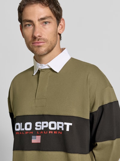 Mężczyzna nosi Relaxed Fit Poloshirt aus reiner Baumwolle od Polo Ralph Lauren, oliwkowa i czarna kolorystyka, nadruk, Nahaufnahme Oberkörper.