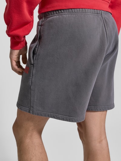 Männermodel trägt Shorts mit Logo Modell 'PLIZZY' von American Vintage, graue Baumwolle, Relaxed Fit, Ganzkörperansicht Rückansicht.