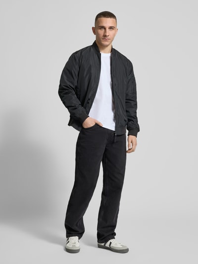 Männermodel trägt Baggy Jeans im 5-Pocket-Design mit Logo-Stitching von KARL KANI in Schwarz auf weißem Hintergrund, Ganzkörperansicht von vorne. Reine Baumwolle, Baggy Fit, Knopf- und Reißverschluss, entspannte Silhouette.