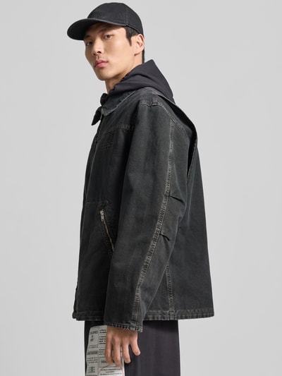 Männermodel trägt Jacke in Denim-Optik mit Umlegekragen von MM6 Maison Margiela, dunkles Grau, Reißverschlusstaschen, Relaxed Fit, Ganzkörperansicht von vorne. Jacke aus reiner Baumwolle; Rückenlänge 74 cm, Schulterbreite 53 cm, Ärmellänge 62 cm bei Größe 50.