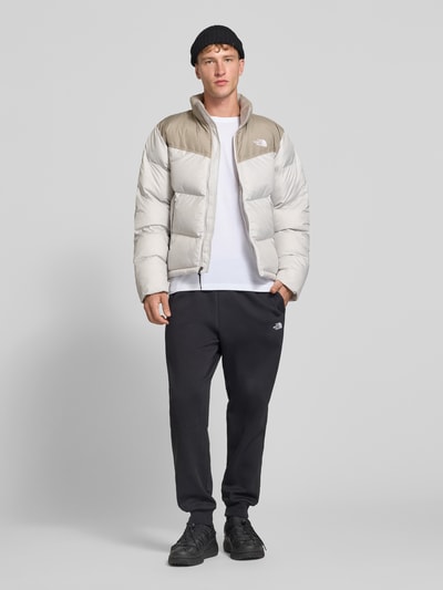 Männermodel trägt Regular Fit Jacke in Stepp-Optik Modell 'SAIKURU' von The North Face in Beige und Hellgrau, Ganzkörperansicht von vorne. Kontext: Damen Jacke von The North Face, Stepp-Optik, Regular Fit, Modell 'SAIKURU', Logo-Stitching, Stehkragen, Rückenlänge bei Größe M: 65 cm, Schulterbreite bei Größe M: 47 cm, Brustweite bei Größe M: 56 cm, Ärmellänge bei Größe M: 67 cm.