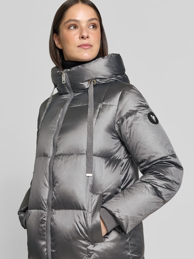 Frauenmodel trägt Mantel mit Entenfederfüllung Modell 'Nova' von MOS MOSH in silbergrau mit Stehkragen und Eingrifftaschen, Nahaufnahme Oberkörper. Damenmantel, Regular Fit, Zweiwege-Reißverschluss, glatte, glänzende Textur.
