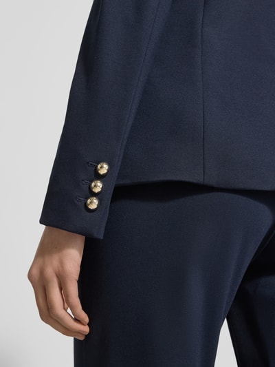 Vrouwenmodel draagt Slim Fit Blazer uit Viscose-mix model 'Ritmo' van Marella, donkerblauw, detailopname mouw en knopen, context: elastische viscose-mix, reverskraag, dubbele knoopsluiting, paspelzakken, ruglengte maat 36: 60 cm, borstwijdte maat 36: 42 cm, mouwlengte maat 36: 58 cm