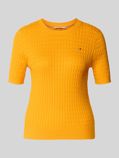 Frauenmodel trägt Slim Fit T-Shirt aus reiner Baumwolle von Tommy Hilfiger, Optik: Unifarben, Zopfmuster, Logo-Detail, Rundhals, Kurzarm, Strick, leuchtend gelb, Struktur durch Zopfmuster, Ganzkörperansicht von vorne.