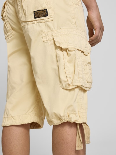 Männermodel trägt Bermudas mit Pattentaschen und Logo-Stitching von Alpha Industries in Beige, reine katoen, straight fit, detailaufnahme Rückansicht
