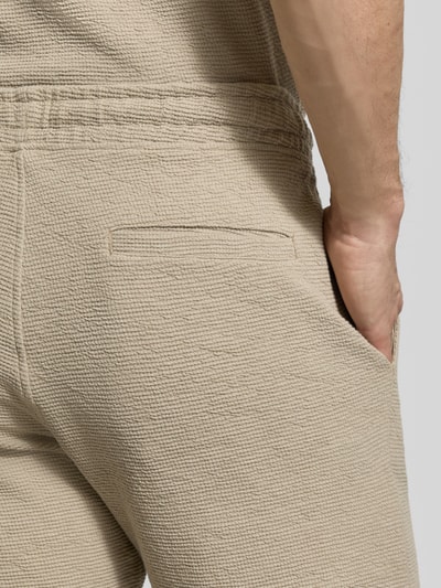 Männermodel trägt Sweatshorts mit elastischem Bund von MCNEAL, Strukturmuster, Eingriff- und Gesäßtaschen, Nahaufnahme Rückansicht.
