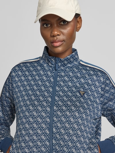 Frauenmodel trägt Regular Fit Sweatjacke mit Allover-Logo-Print von GUESS in Blau mit weißem Muster, elastischer Material-Mix, Nahaufnahme Oberkörper.
