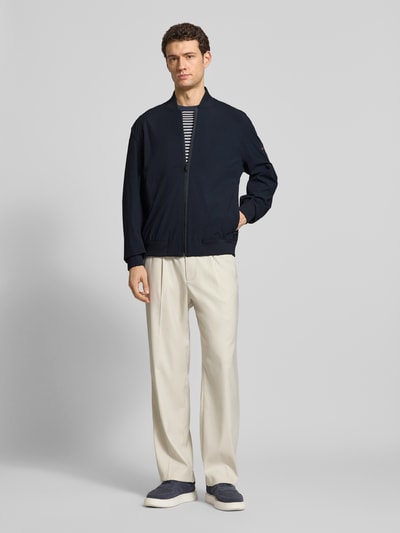 Männermodel trägt Regular Fit Blouson mit Baseball-Kragen Modell 'OSURF' von BOSS Orange, unifarben, Reißverschluss, Ganzkörperansicht von vorne.