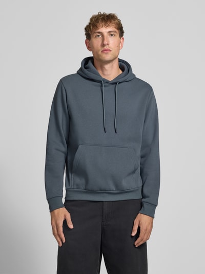 Männermodel trägt Hoodie mit Känguru-Tasche Modell 'BRADLEY' von JACK & JONES in Grau, lockerer Schnitt, Ganzkörperansicht von vorne.