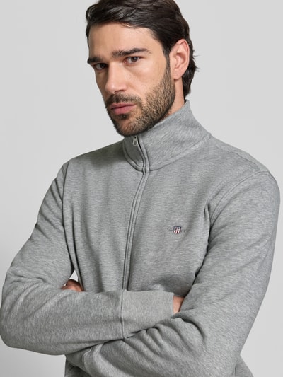Männermodel trägt Regular Fit Sweatjacke mit Stehkragen Modell 'Gield' von Gant, grau, Logo-Stitching, Nahaufnahme Oberkörper. Baumwoll-Mix, Reißverschluss, elastische Abschlüsse.