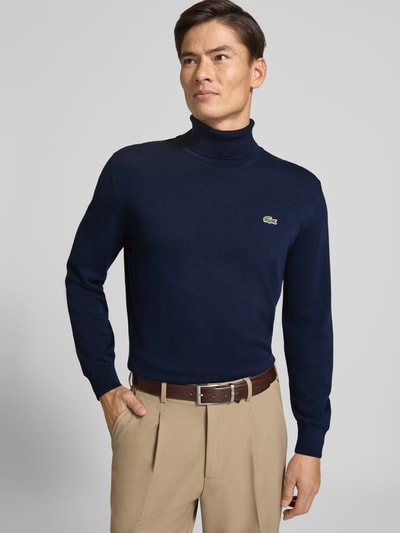 Männermodel trägt Regular Fit Pullover aus reiner Baumwolle von Lacoste, dunkelblau, mit glatter Textur, Ganzkörperansicht von vorne, Herren Turtleneck-Pullover von Lacoste.