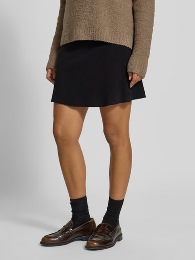 Kobieta-modelka nosi czarną spódnicę mini z mieszanki wiskozy model 'SABA' od VERO MODA, damska spódnica mini, zdjęcie całej sylwetki z przodu.