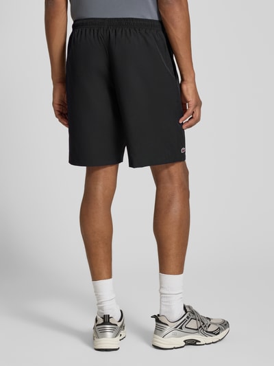 Männermodel trägt schwarze Relaxed Fit Shorts mit Logo-Patch von Lacoste, Herren Sportshorts, locker geschnitten, Ganzkörperansicht Rückansicht.