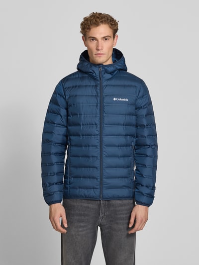 Męski model nosi kurtkę pikowaną z efektem pikowania, krój regular fit, Model 'Lake 22™' od Columbia, Kaptur, nadruk z logo, zamek błyskawiczny, długość tyłu w rozmiarze M: 72 cm, szerokość ramion w rozmiarze M: 43 cm, szerokość klatki piersiowej w rozmiarze M: 42 cm, długość rękawów w rozmiarze M: 70 cm, niebieski kolor, faktura gładka, widok całej sylwetki z przodu.