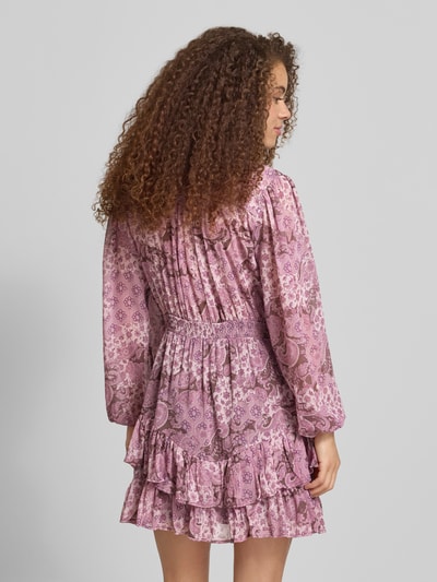 Frauenmodel trägt Minikleid mit Paisley-Muster im Stufen-Look von Review in Rosa- und Lilatönen, Ballonärmel, recyceltes Polyester, Ganzkörperansicht Rückansicht