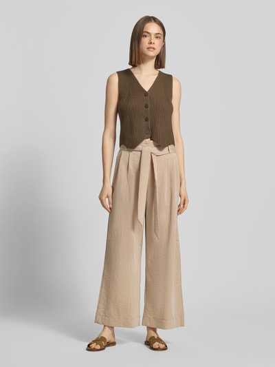 Frauenmodel trägt Regular Fit Bundfaltenhose aus Viskose-Mix Modell 'MARSA' von Only in Beige mit Bindegürtel und Rüschen, ganzkörperansicht von vorne.